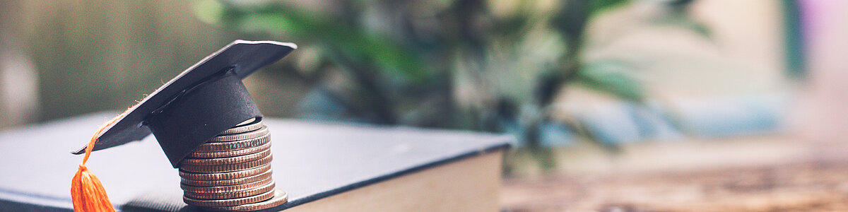 Buch mit Münzen und Akademikerhut
