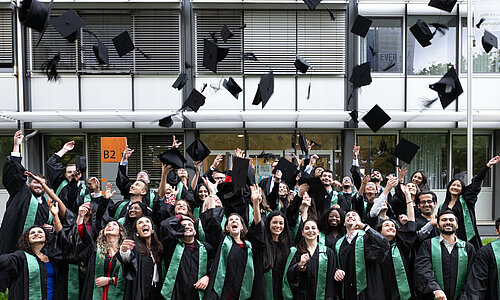 Gruppenbild von Absolventen, die ihren Akademikerhut in die Luft werfen 